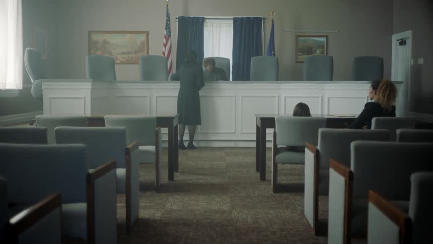 A lawyer talks to a judge at her bench as a woman and child sit and wait
