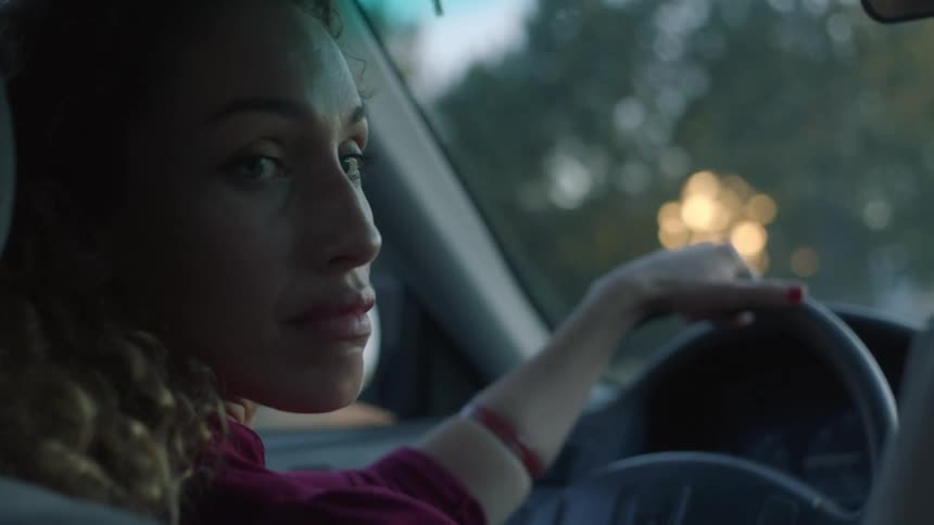 Young woman driving a car on a neighborhood at sunrise