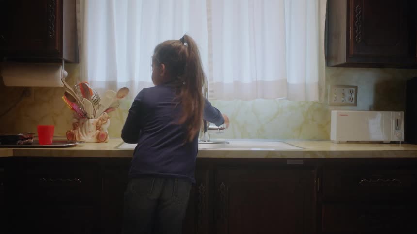 A little girl pouring water from a faucet in the kitchen into cups