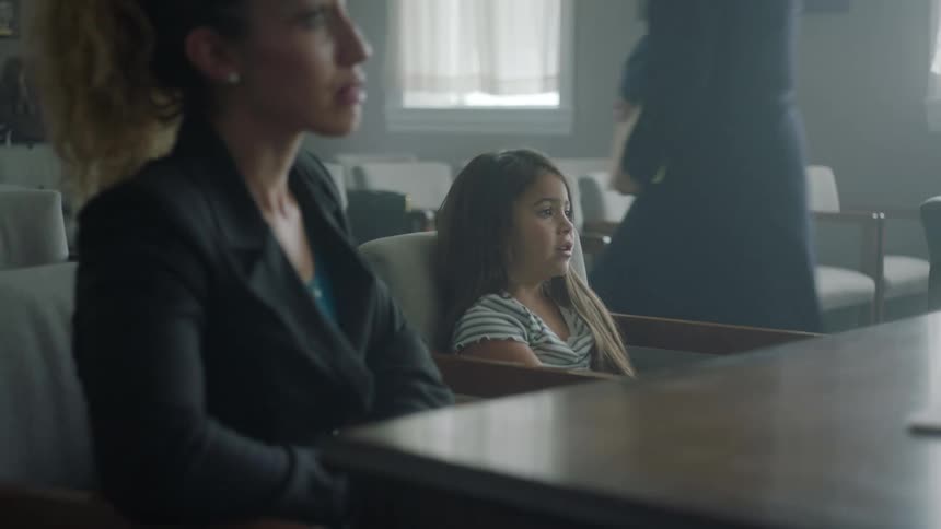 A girl and her guardian sitting in front of a desk in a dimly lit office