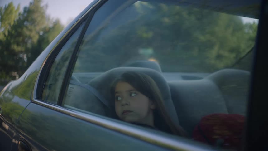 A young girl looks out the window of a moving car at the passing trees