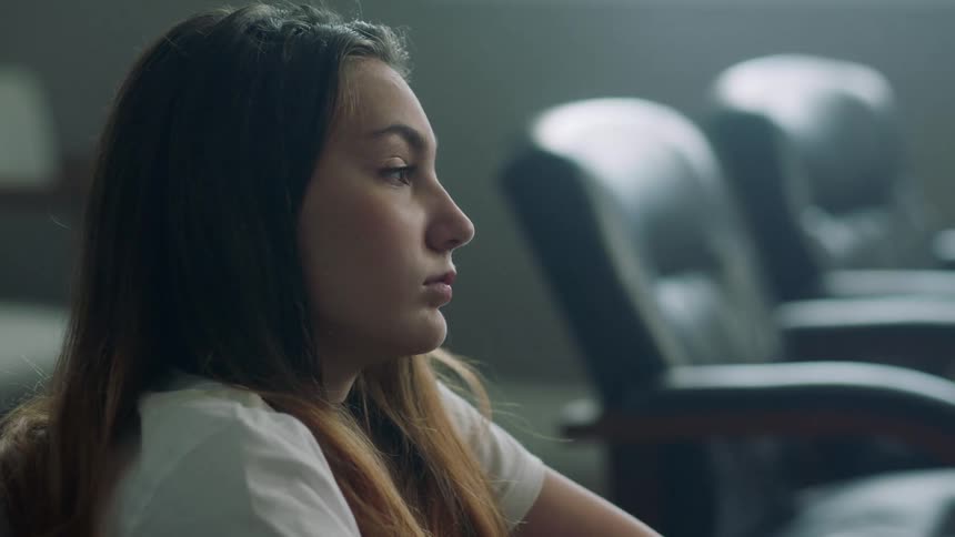 A young woman with brown hair sits in a room with a number of leather office chairs