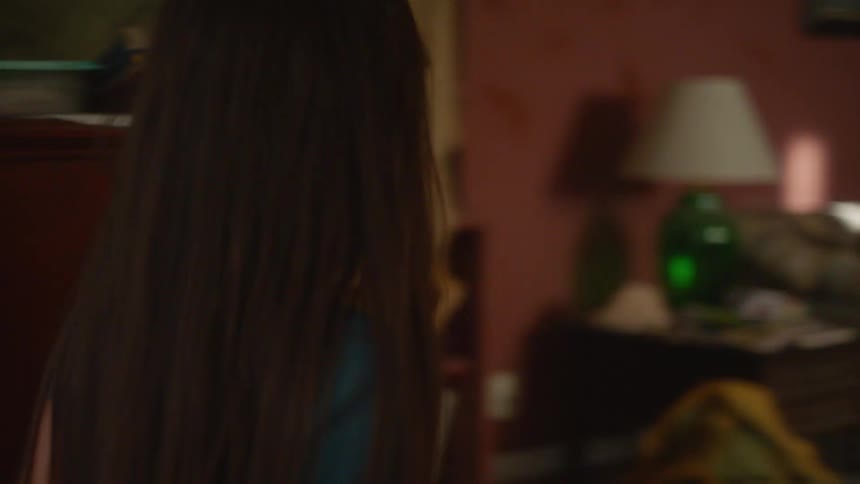 A young girl trudges through a messy house and approaches her mother who is resting on the living room couch