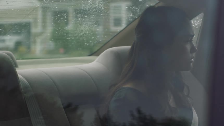 A female teenager sits in the back of a car driving through a neighborhood