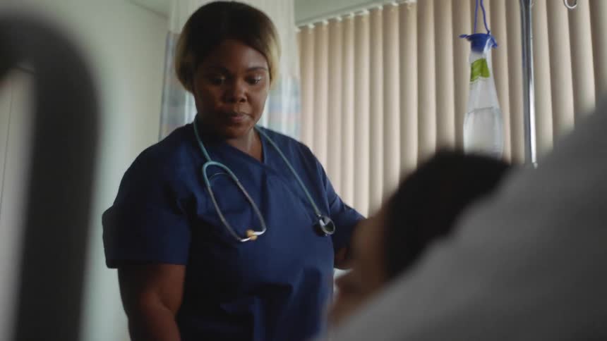 A woman laying in a hospital bed as a nurse with a stethoscope checks her iv