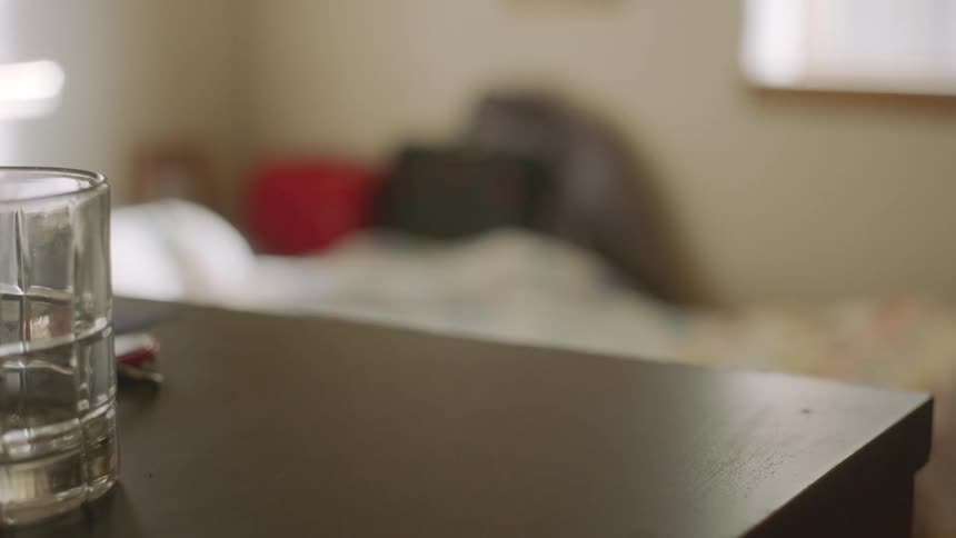 Woman scoops a few bottles of prescription medication into a bag from off a dresser