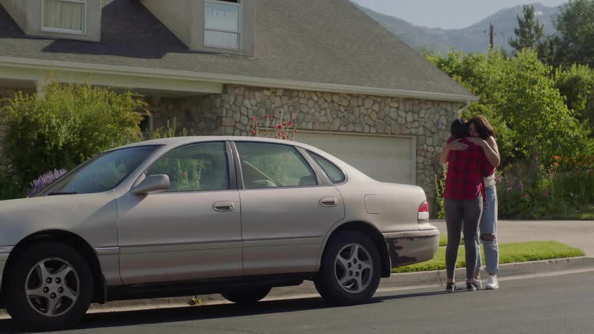 Two women hug each other while standing in the street near a parked car