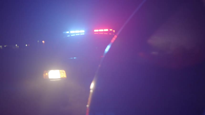 Police lights flash as a young girl gets out of a car and runs behind it where a police officer stops her