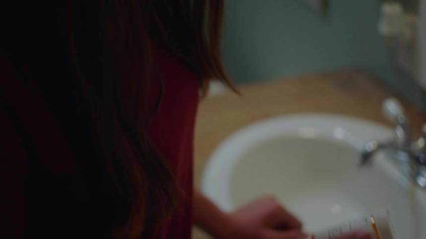 A woman standing in a bathroom picks up and looks at a prescription pill bottle