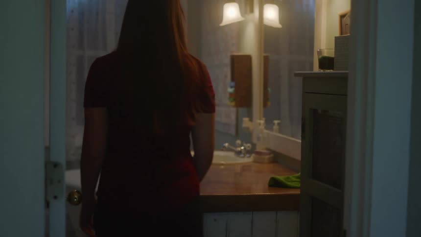 Young long haired woman enters the bathroom at home in the evening