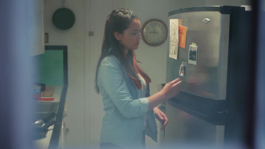 Woman closes a refrigerator door and then picks up a photo from the front of the fridge and stares at it