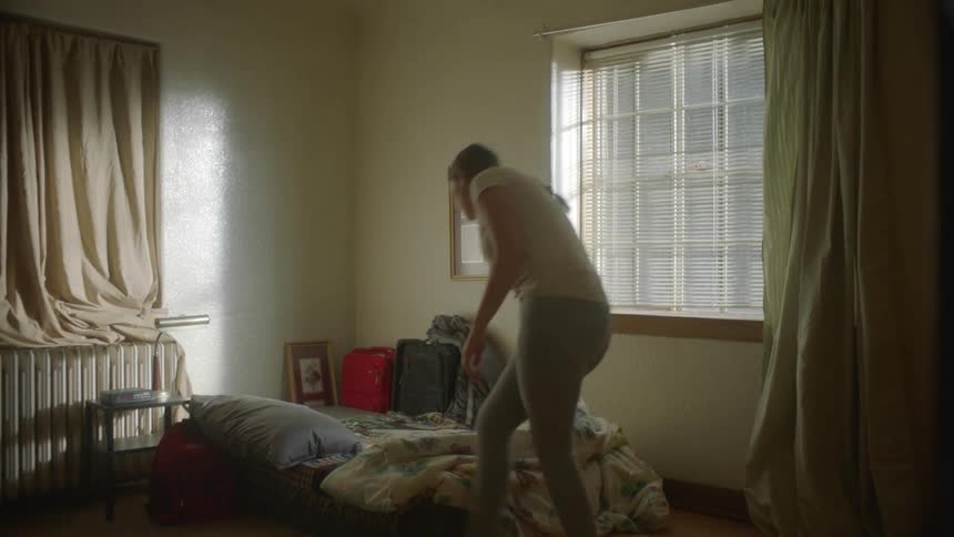 A female in a bedroom making a bed and drawing curtains