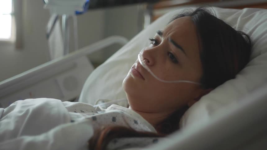 A woman is lying in a hospital bed with an oxygen tube in her nose