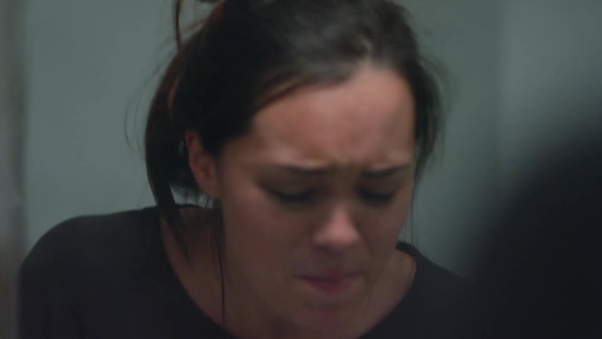 A woman takes pills from a bottle and swallows water from a glass in front of a mirror