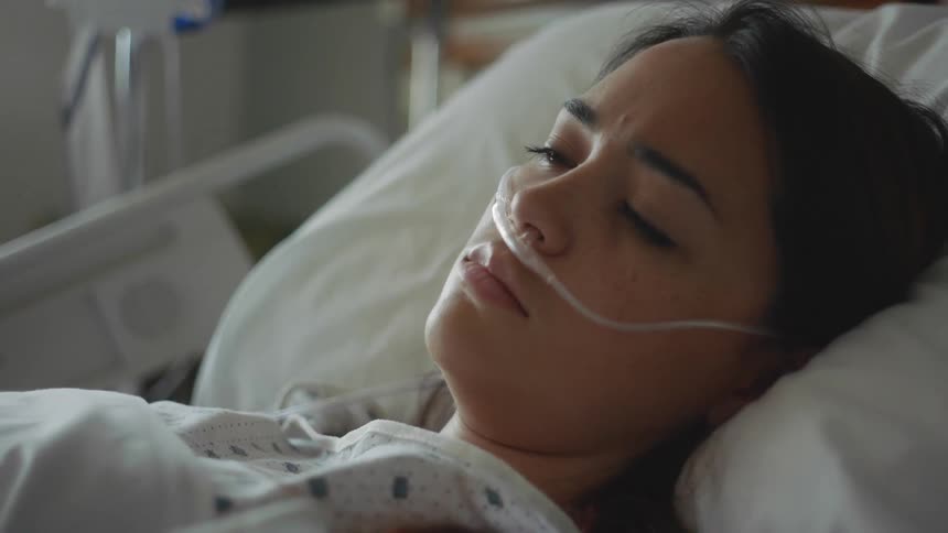 Woman lays in a hospital bed with an oxygen tube in her nose