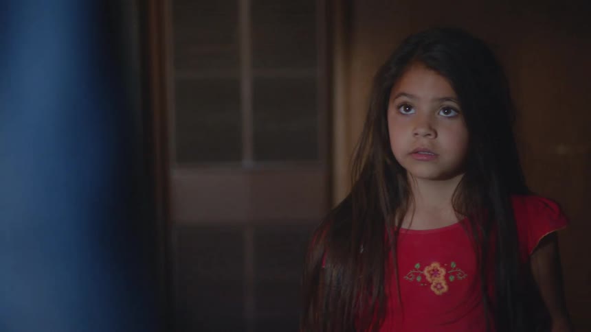 A young girl cowers in fear as her father corners her in a hallway