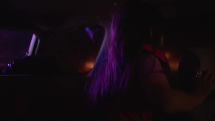A woman driving a car is pulled over by police with the officer shining a flashlight into the backseat to show a little girl