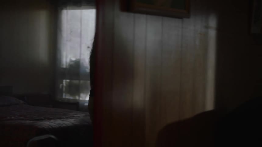 Woman opens door to receive a delivery while her daughter waits sitting in the floor of a dimly lit house