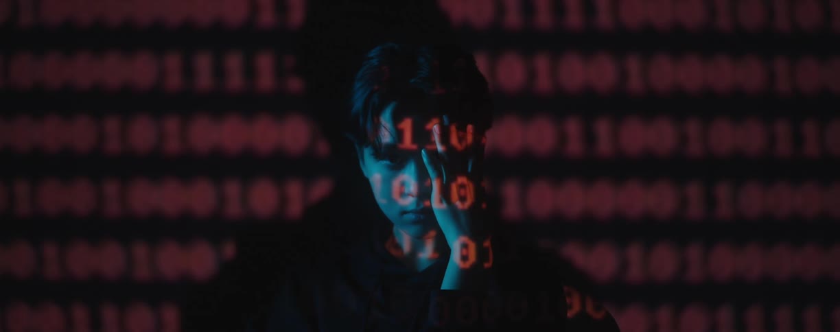An asian man sits with his hand to his face with red numbers displayed in lights