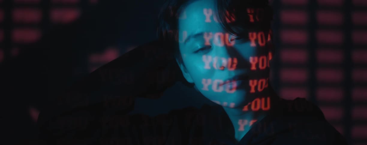 Red text projected over the face of a young woman in a dark room