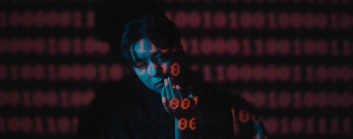 A young woman extends her hand outward in a dark room with red words projected onto her