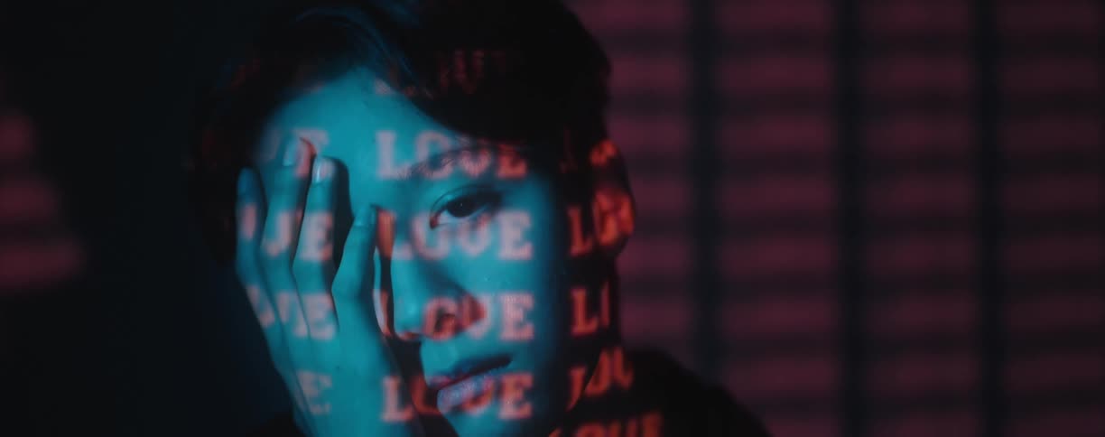 An asian man places his hand to his face as red lighted text displays over him