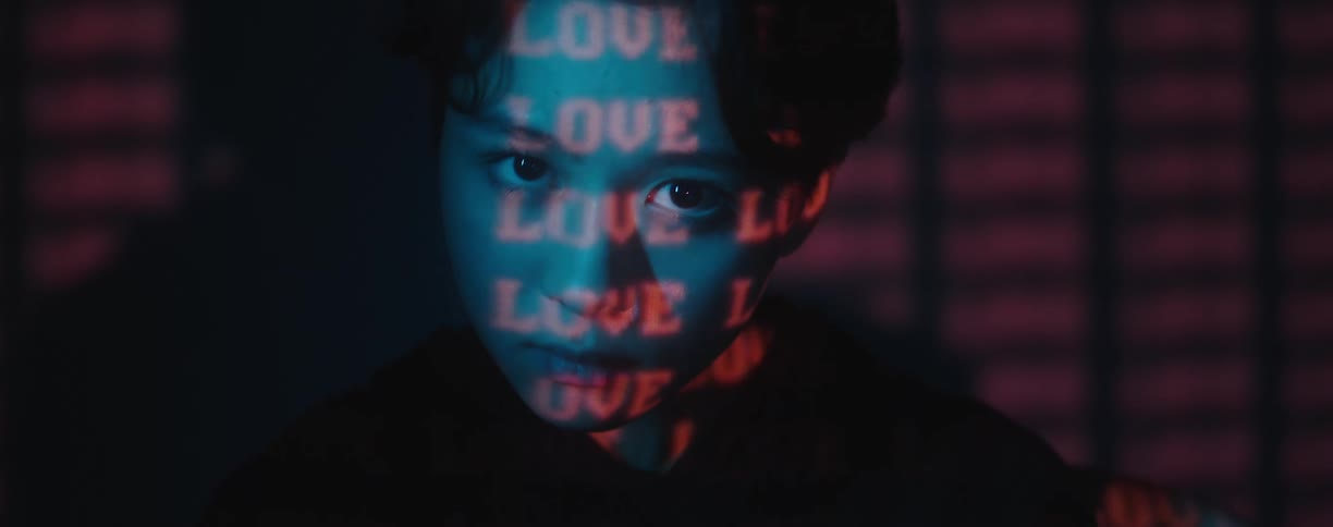 The word love is projected on the face of a model standing in front of a digital screen