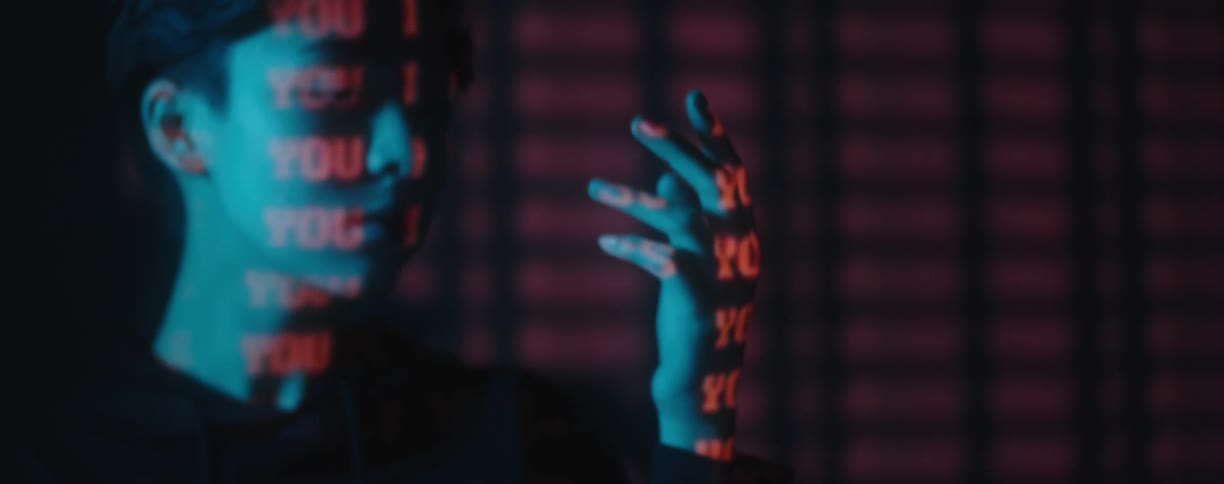 A woman holds her hand up while in a dark room with red words projected onto her
