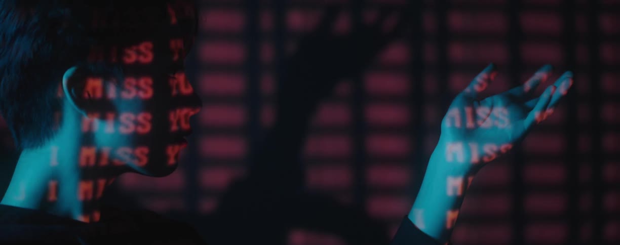 A woman holds her hand up and moves it around while in a dark room with red words projected onto her