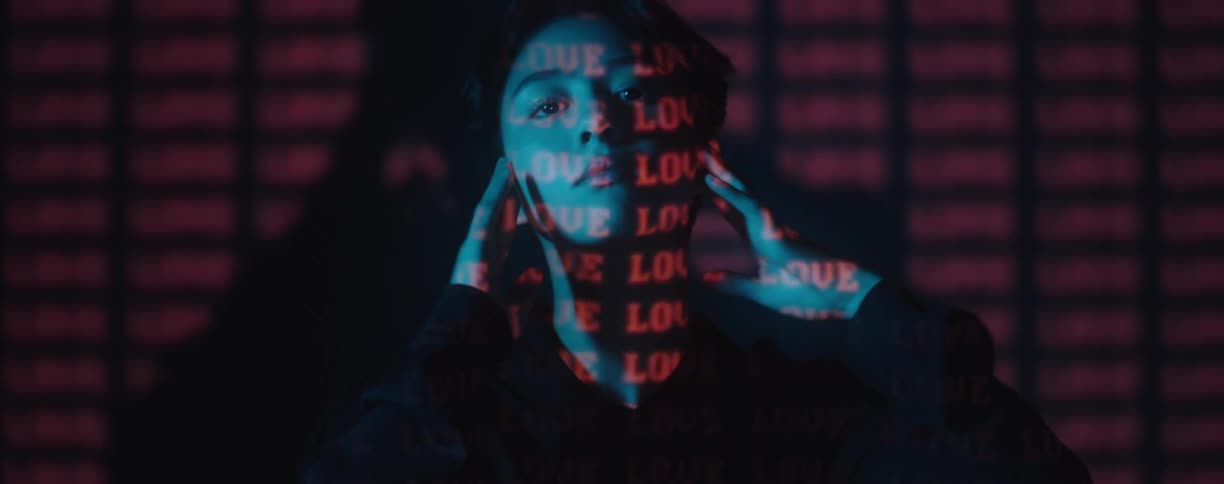 Close up of red text projected over the face and hands of a young woman in a dark room
