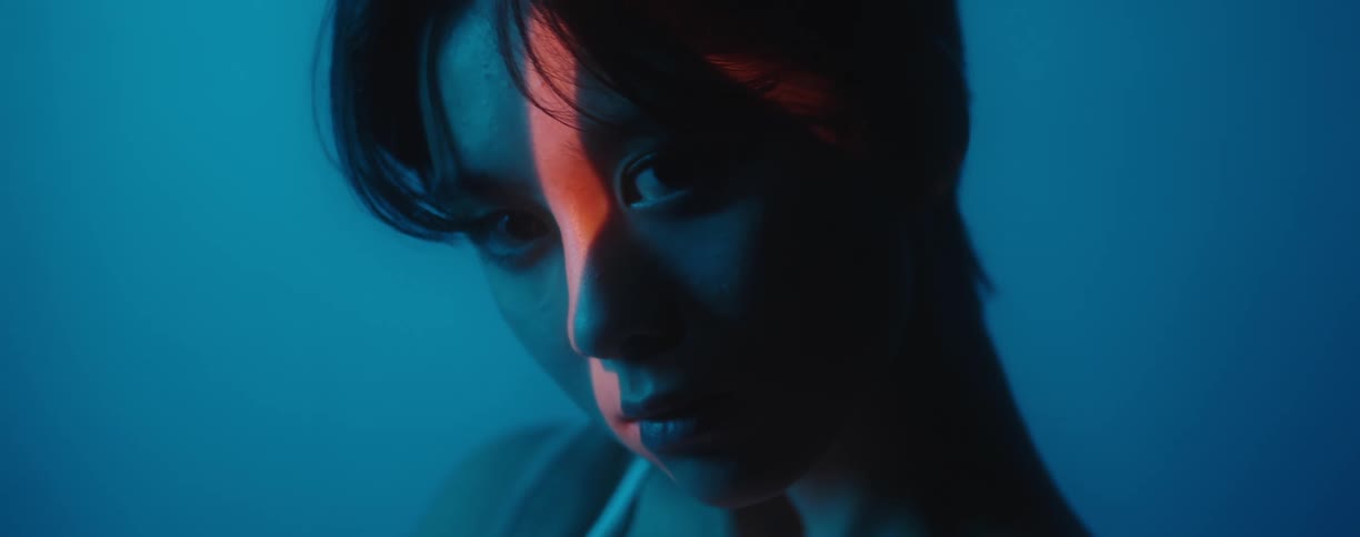 A woman stares straight ahead in shadows with a red light reflecting on her face