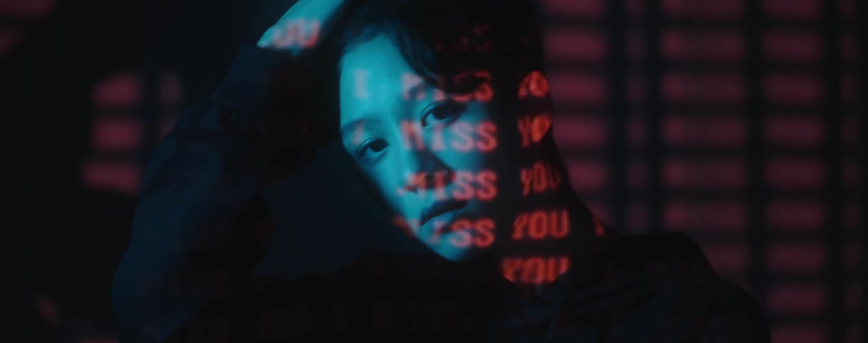 The words i miss you are projected in red in a dark room while woman poses