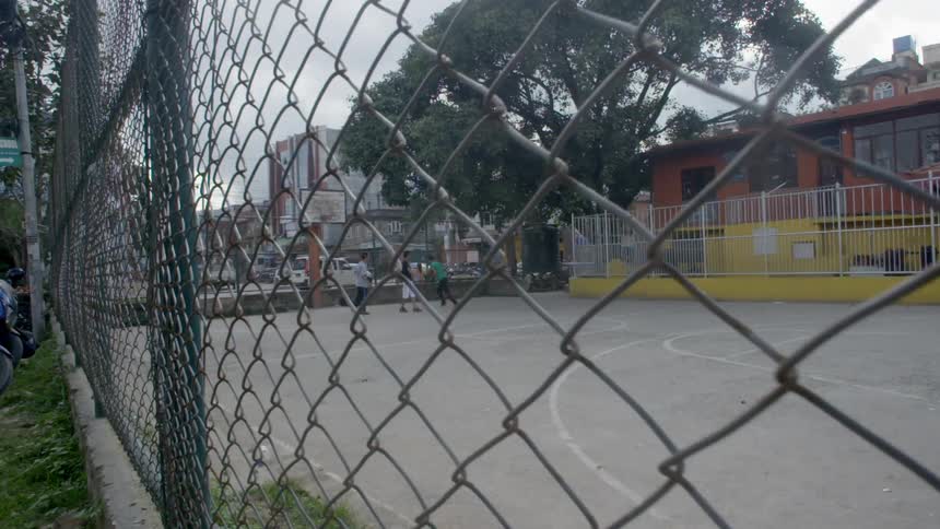 Close up of a fence with people playing basketball on a court inside