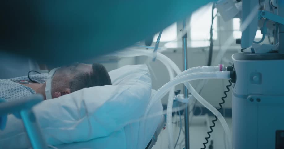 Nurses tending to a male patient asleep in a hospital bed