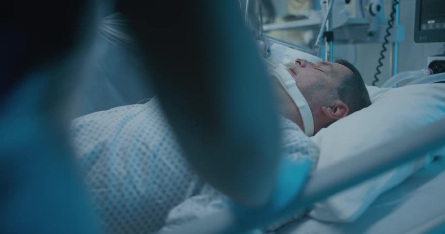 Nurses stand next to a hospital bed with a man lying in it
