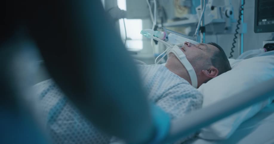 A male patient sleeping in a hospital bed while hooked up to medical equipment