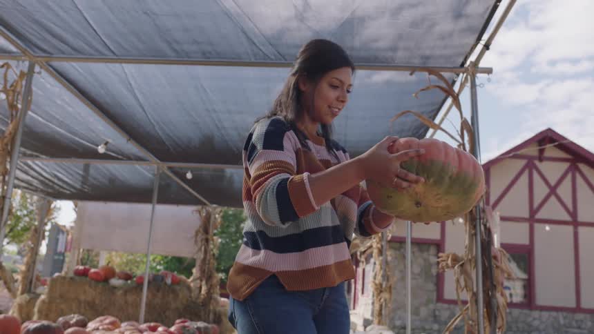A woman picking out a pumpkin at an outdoor pumpkin patch on a fall day