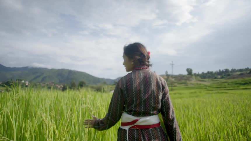 Asian woman walking through tall grass on a cloudy day