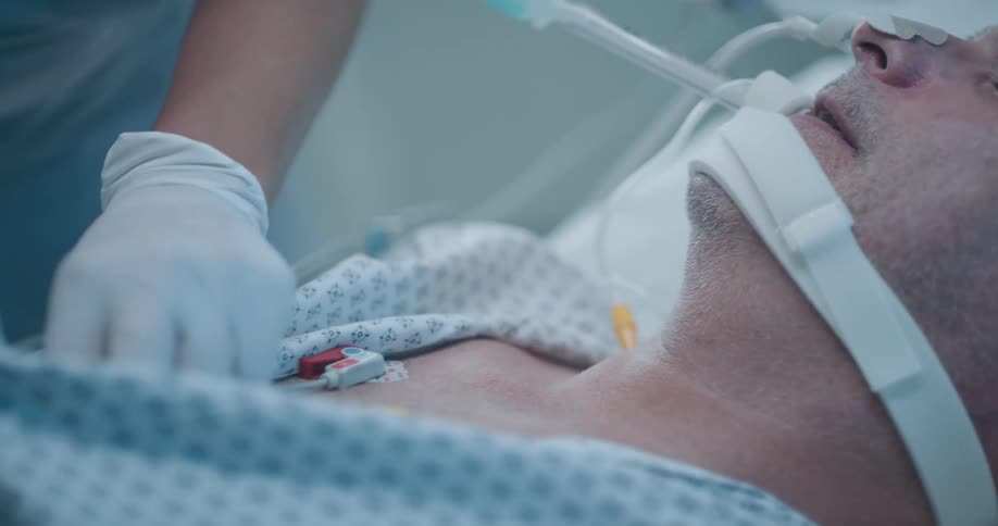 A nurse attaches medical equipment to an unconscious patient in a hospital bed