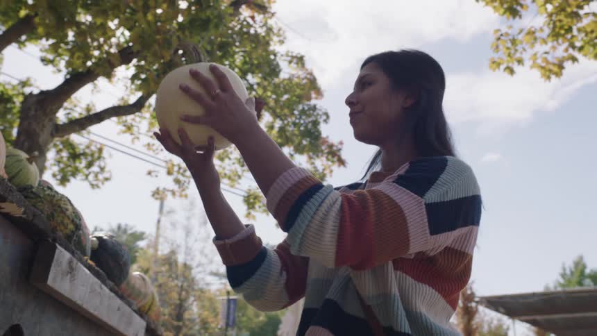 A young woman picks up a white pumpkin and smiles while examining it