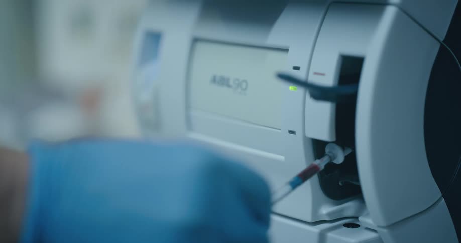 A nurse inserts a syringe of blood into a medical machine