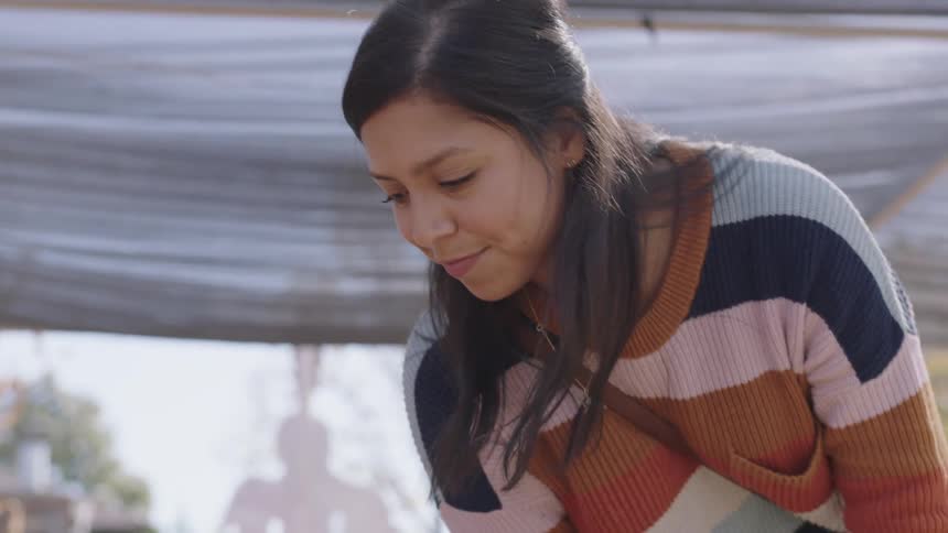 Brunette woman with dark straight hair chooses a pumpkin to buy in the market