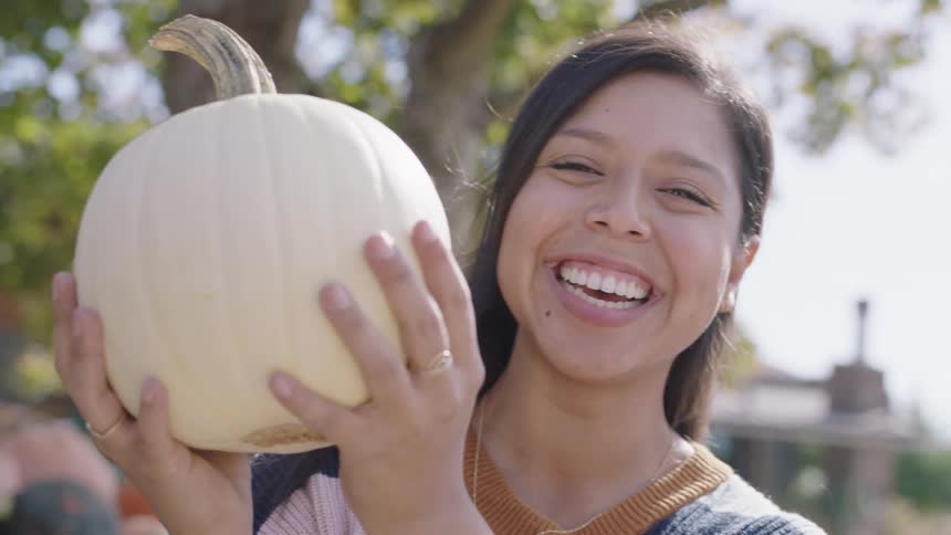 A smiling female holding up a pumpkin outdoors