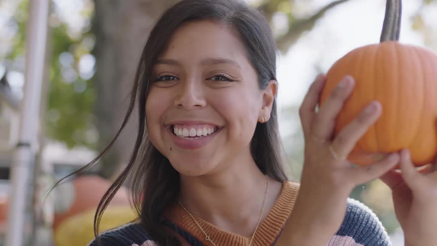 A woman smiling while holding a pumpkin in front of her face