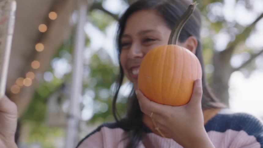 A young woman smiles and takes a selfie while holding a pumpkin