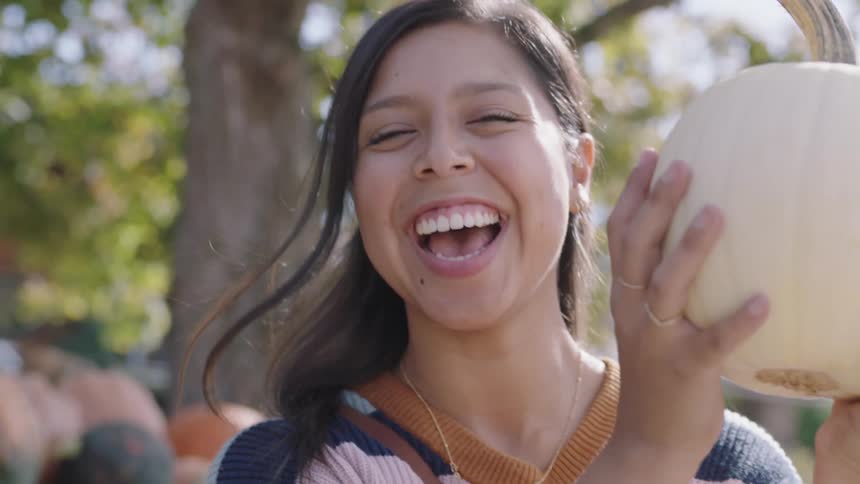 A woman is holding a pumpkin outdoors and smiling
