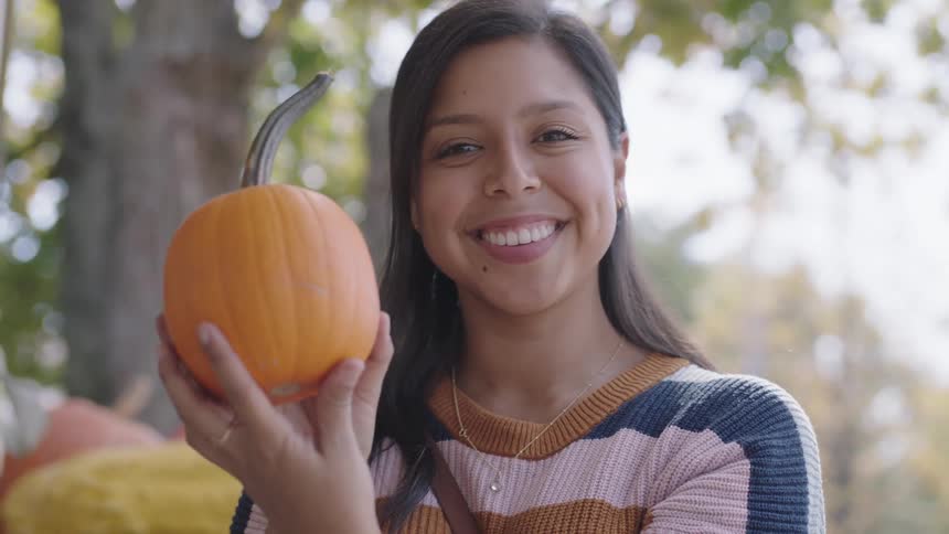 A young woman smiles after examining a pumpkin