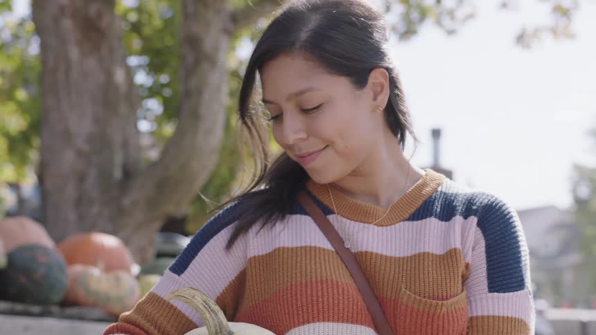 A woman holding a white pumpkin looks down at it while smiling