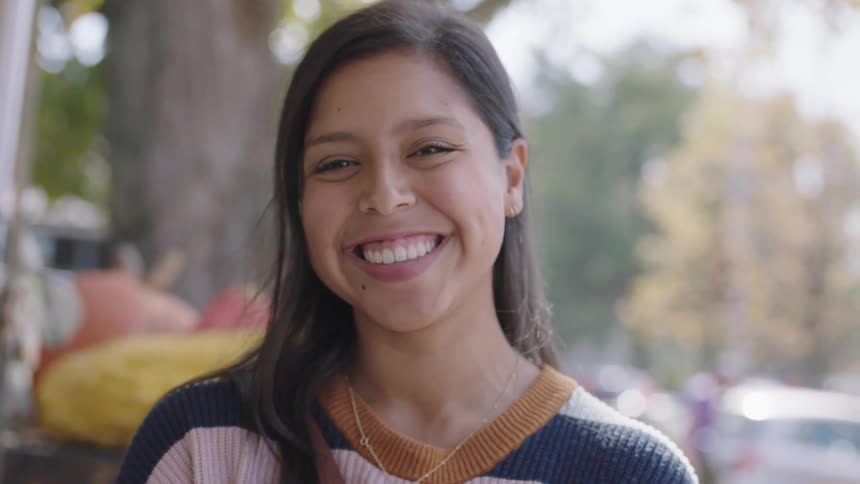 A teenage girl laughs as she removes a pumpkin from in front of her face