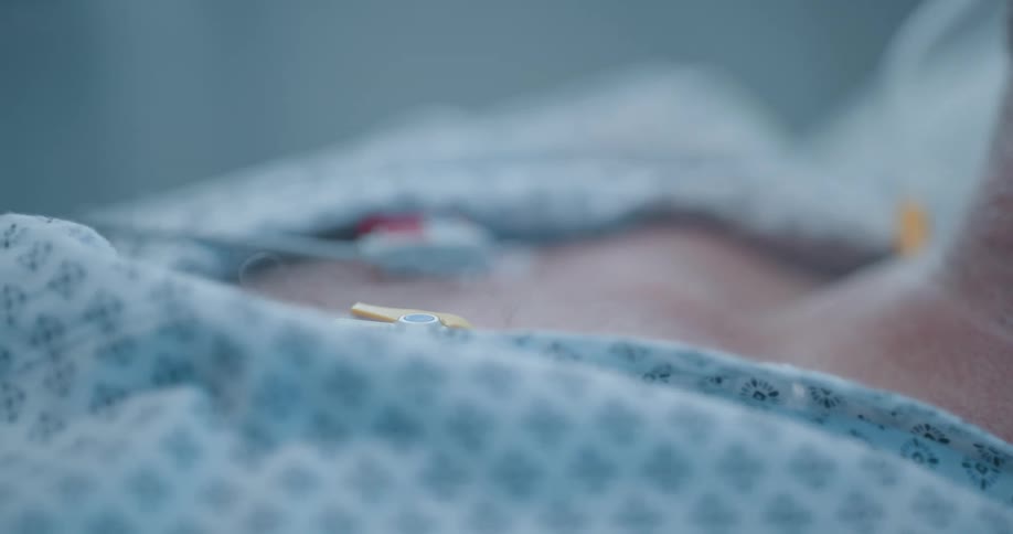 Doctor checks vitals of an unconscious intubated man laying on a hospital bed